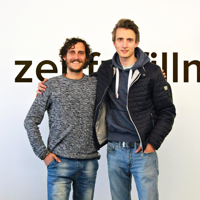 Die beiden Gründer von Zenfulfillment vor einer weißen Wand auf der das Firmenlogo zu sehen ist.